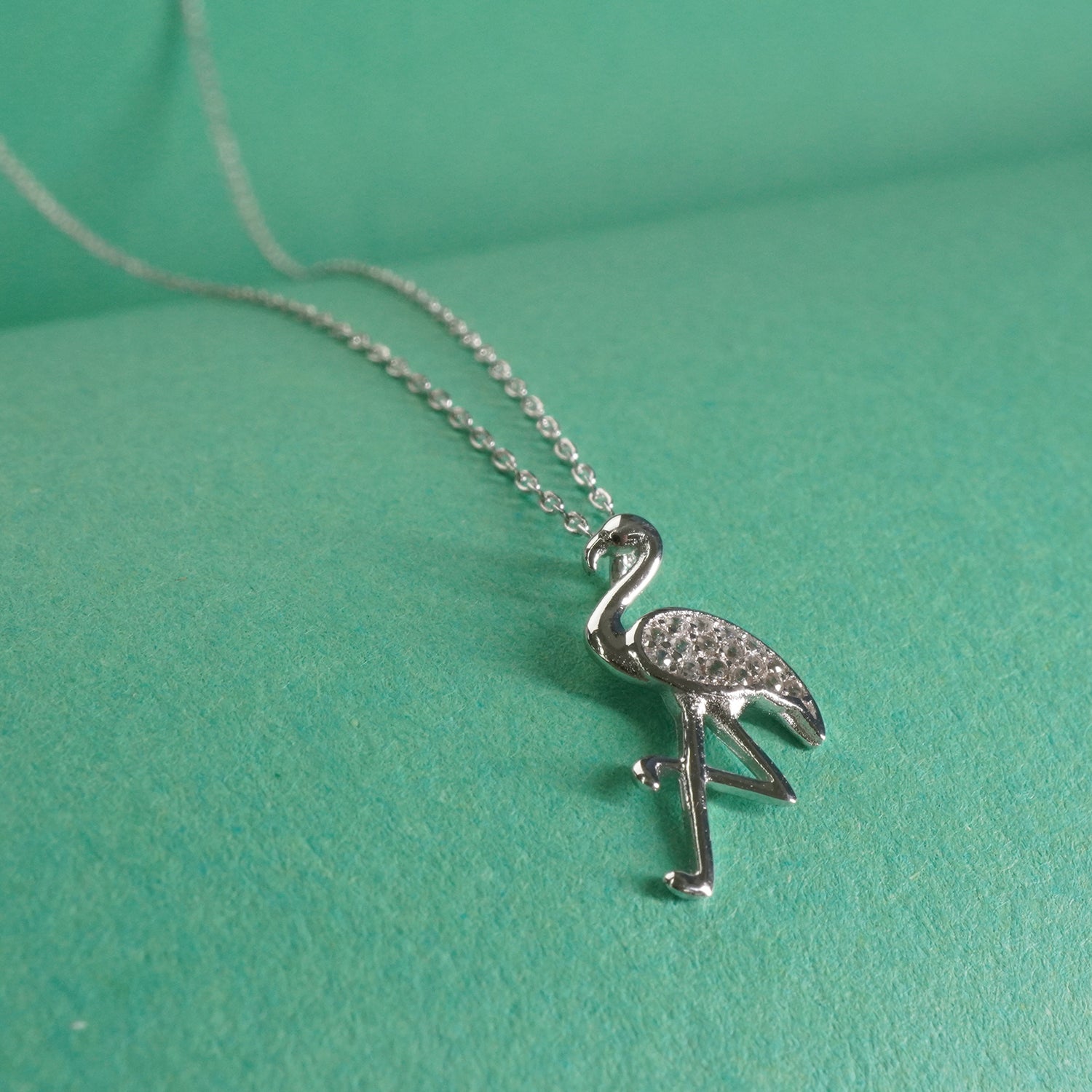 Silver flamingo pendant necklace on a green background