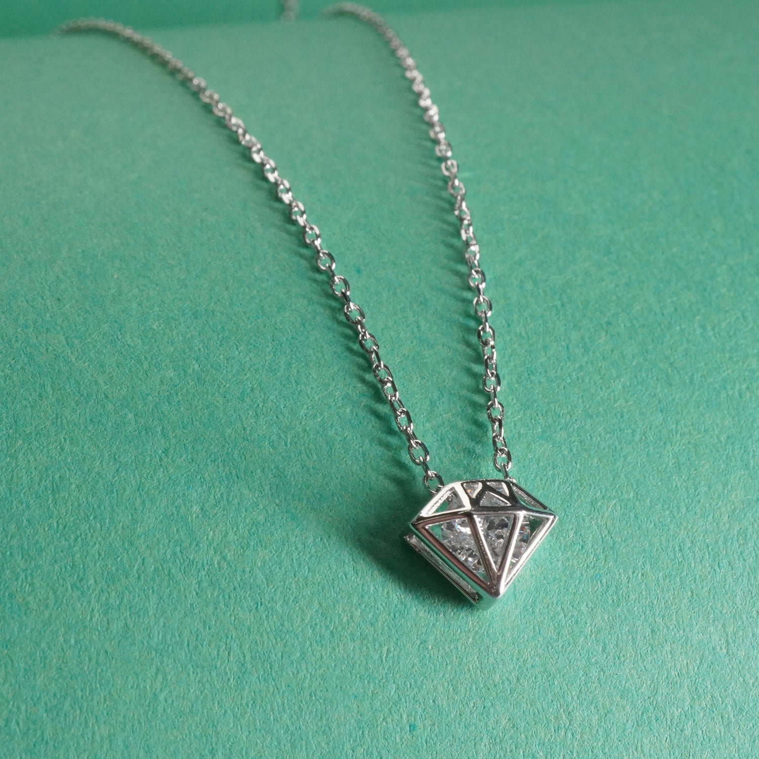 92.5 sterling Silver necklace with a diamond shaped 
pendant on a teal background