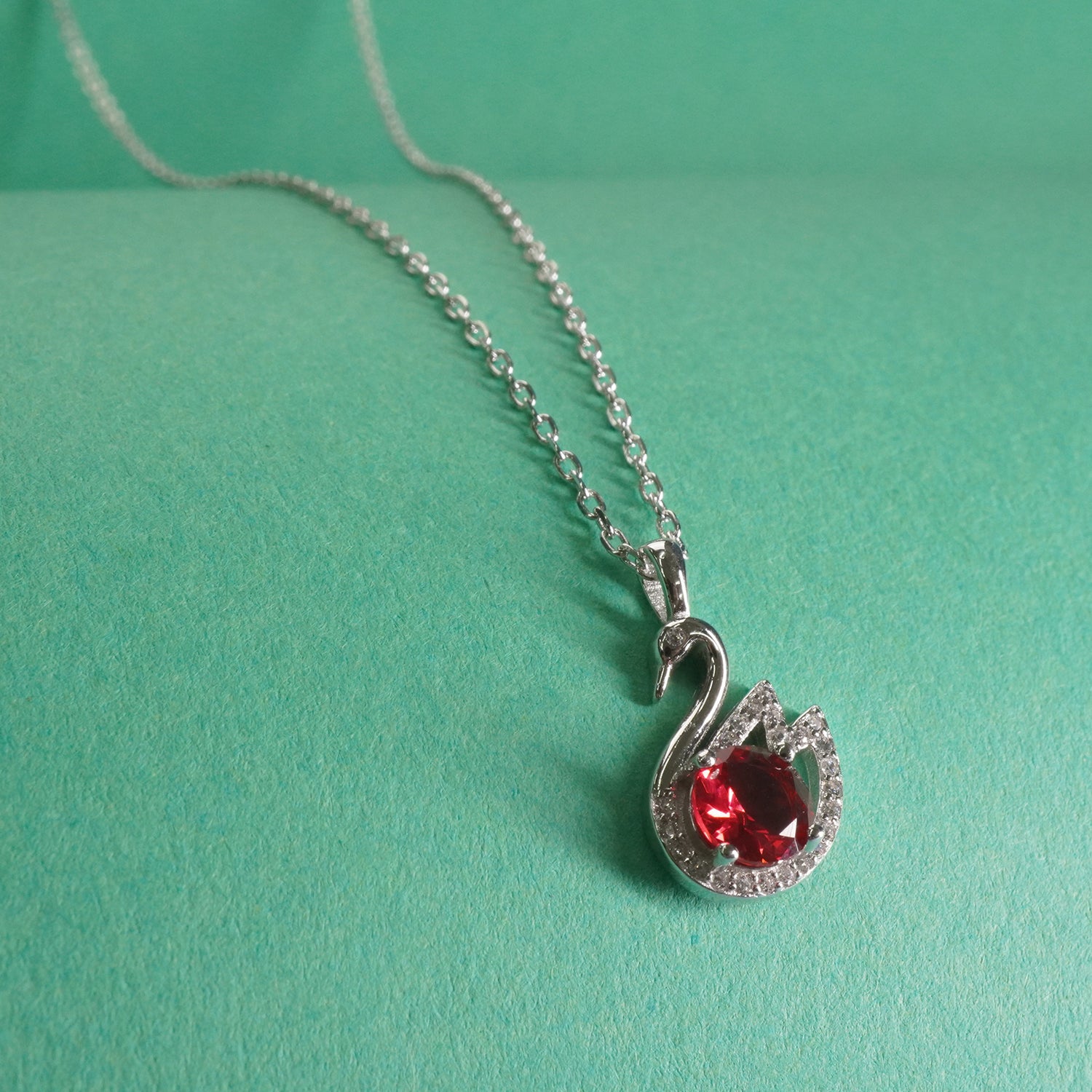 Silver swan necklace with a red gemstone on a green background