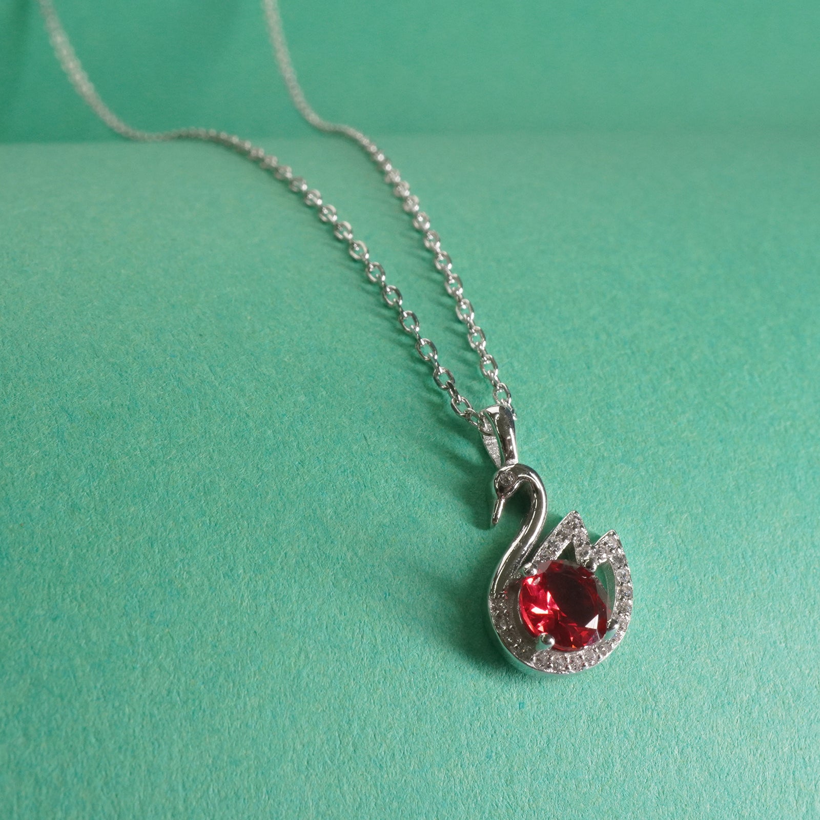 Silver swan necklace with a red gemstone on a green background
