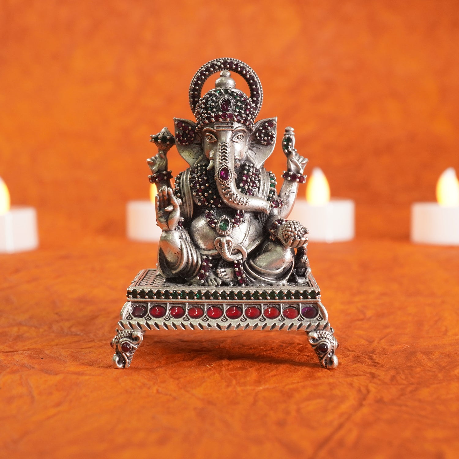 Decorative statue of ganpataji on an orange background with candles