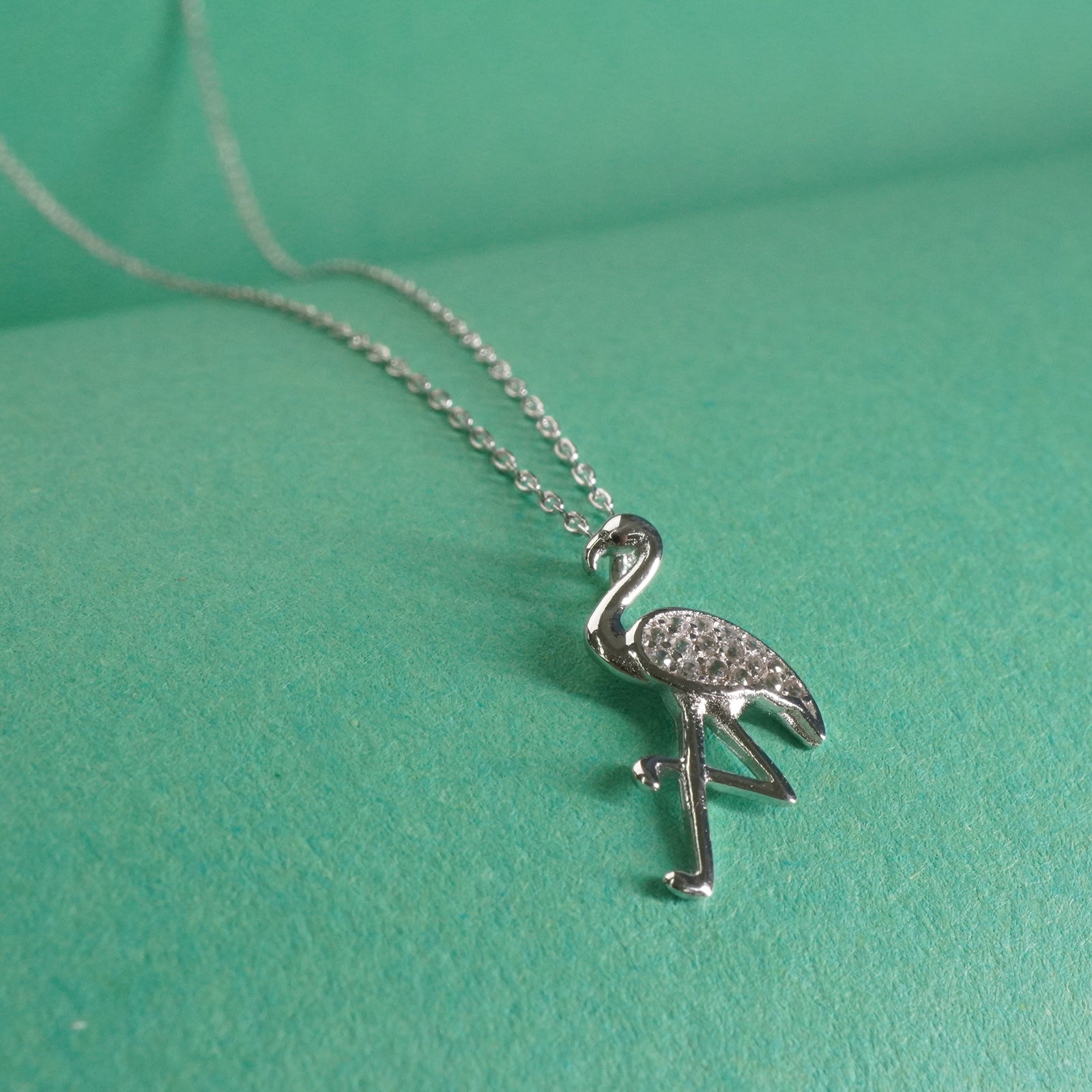 Silver flamingo pendant necklace on a green background